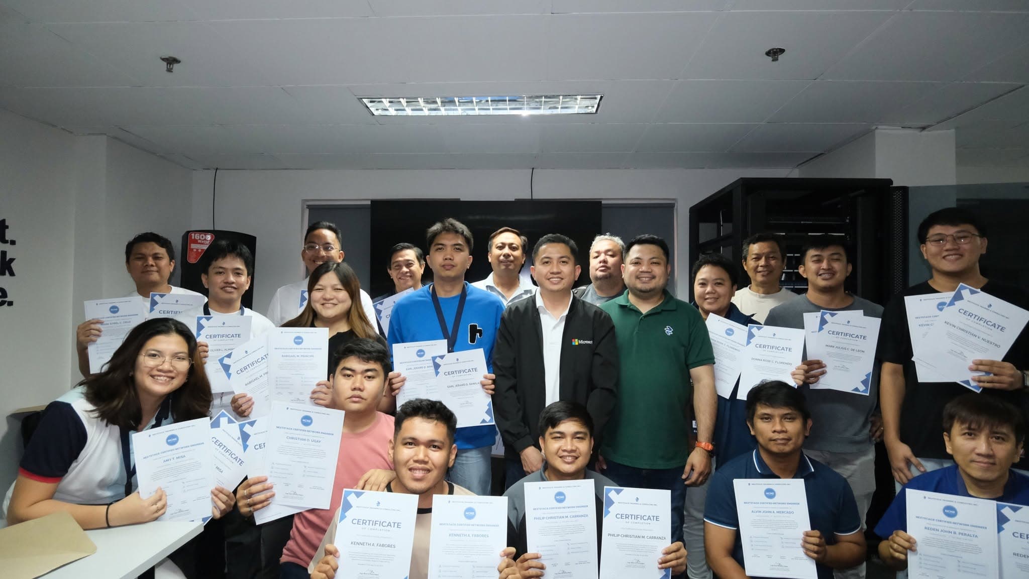 A large group of participants standing together, each holding a NextStack Certified Network Engineer certificate of completion.