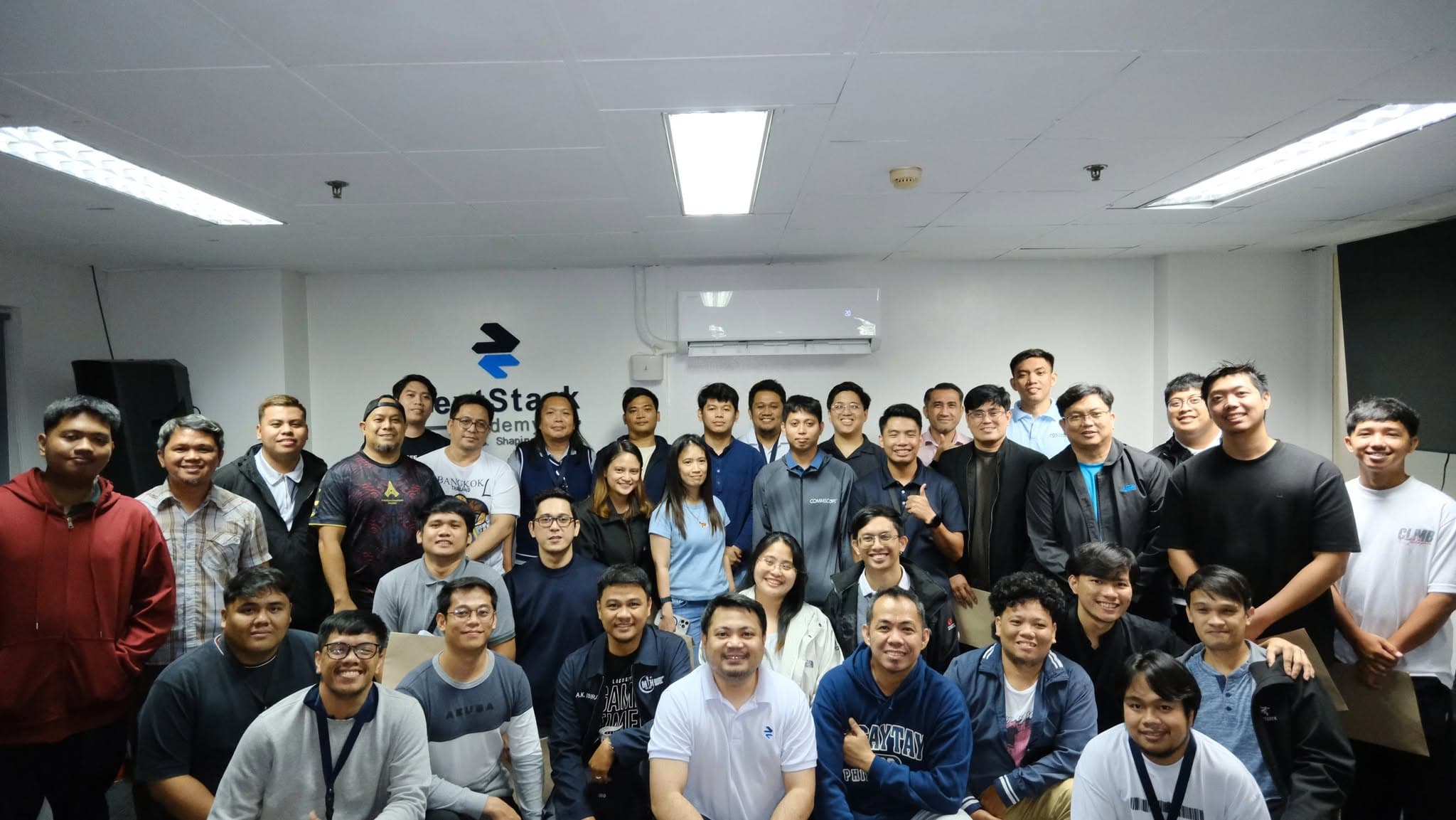 A large cohort of participants gathered for a group photo beneath the NextStack Academy wall sign.